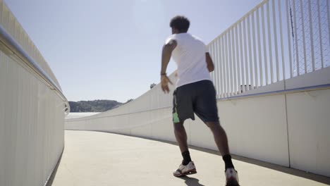Rear-view-of-sporty-African-American-man-running-on-bridge.